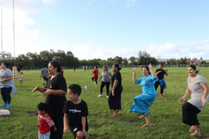 Families and community members, including women and children, taking part in an energetic outdoor Zumba session on a wide open field.