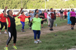 Women of different ages joining a lively Zumba class outdoors, following the instructor’s movements on a community field.